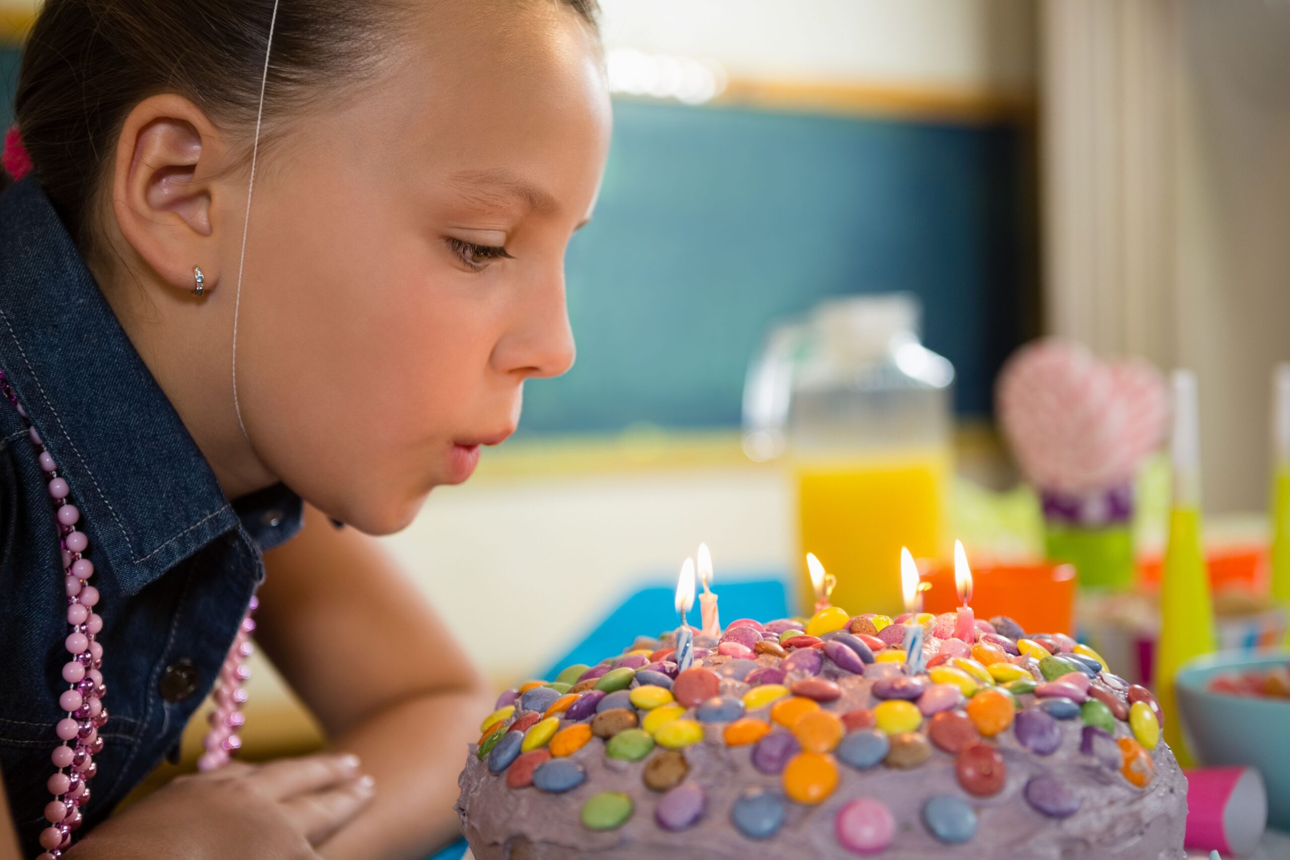 a tween girl blowing out candles on a candy dotted cake. continue reading for the how to plan a birthday party checklist