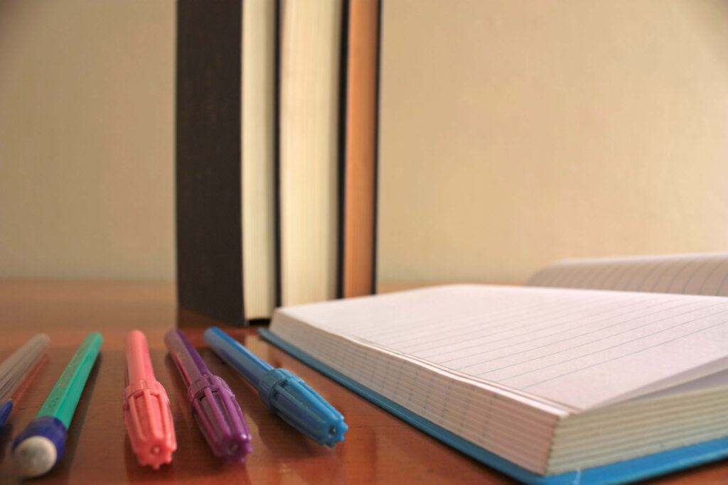 markers, pen and pencil lay in a straight row next to a notebook to represent an organized life.