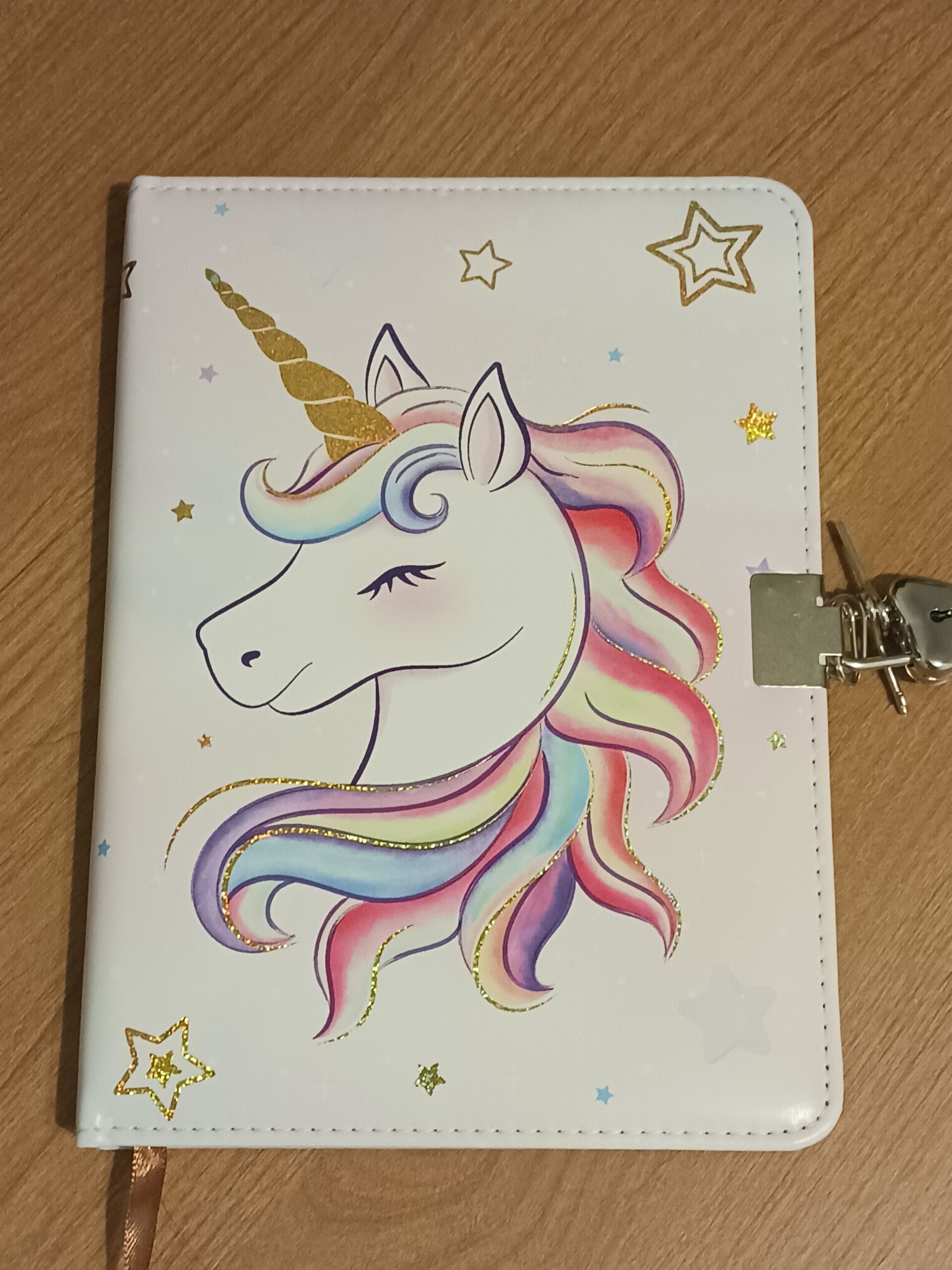 a white unicorn journal, the unicorn has a rainbow mane and stars and dots are scattered on the cover. This journal has keys and a lock.