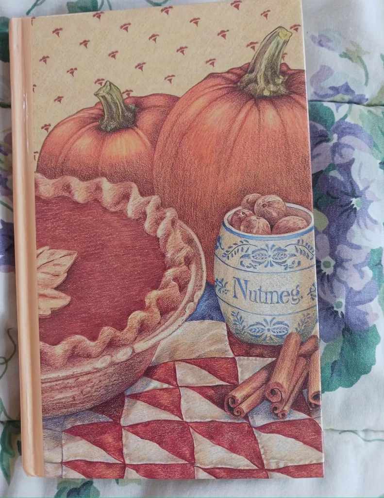 my autumn kitchen journal, the cover has beautiful art of a pumpkin pin, bowl of nutmeg shells, cinnamon sticks and 2 large pumpkins